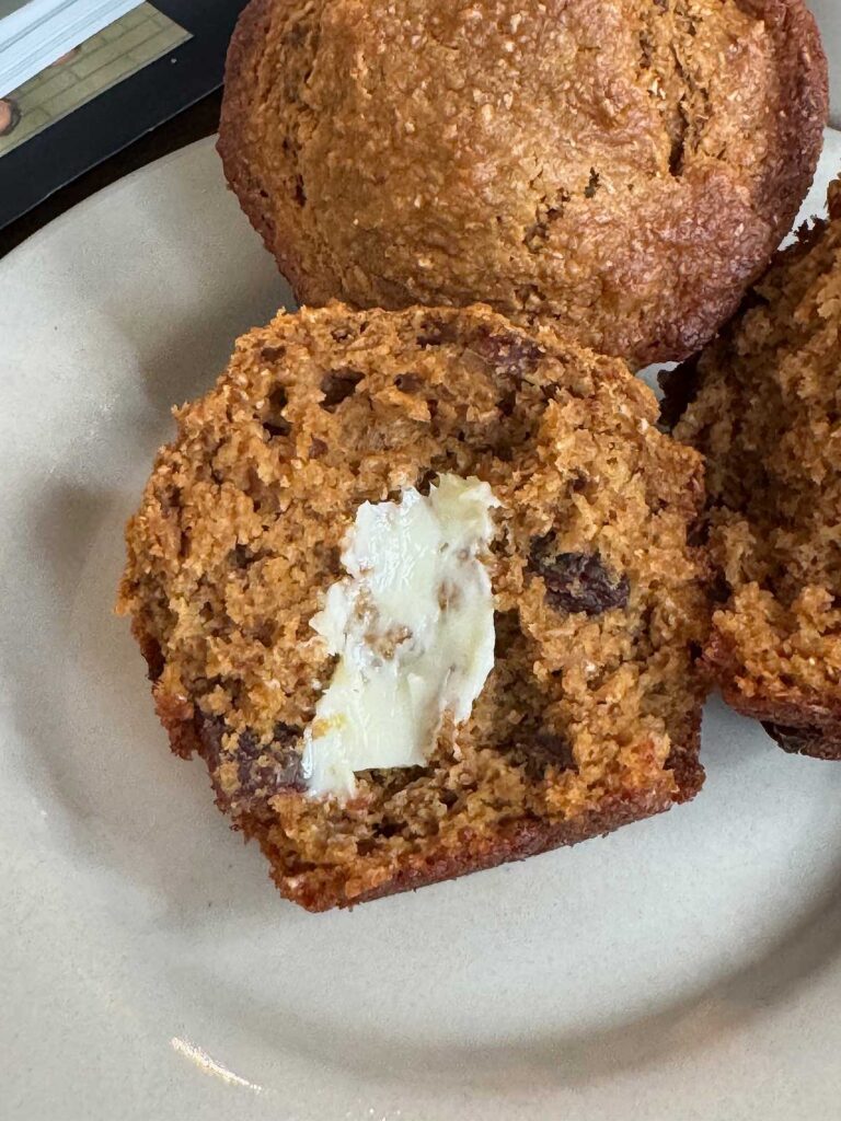A basic bran muffin made with coarse wheat brand and molasses split to show texture with butter.