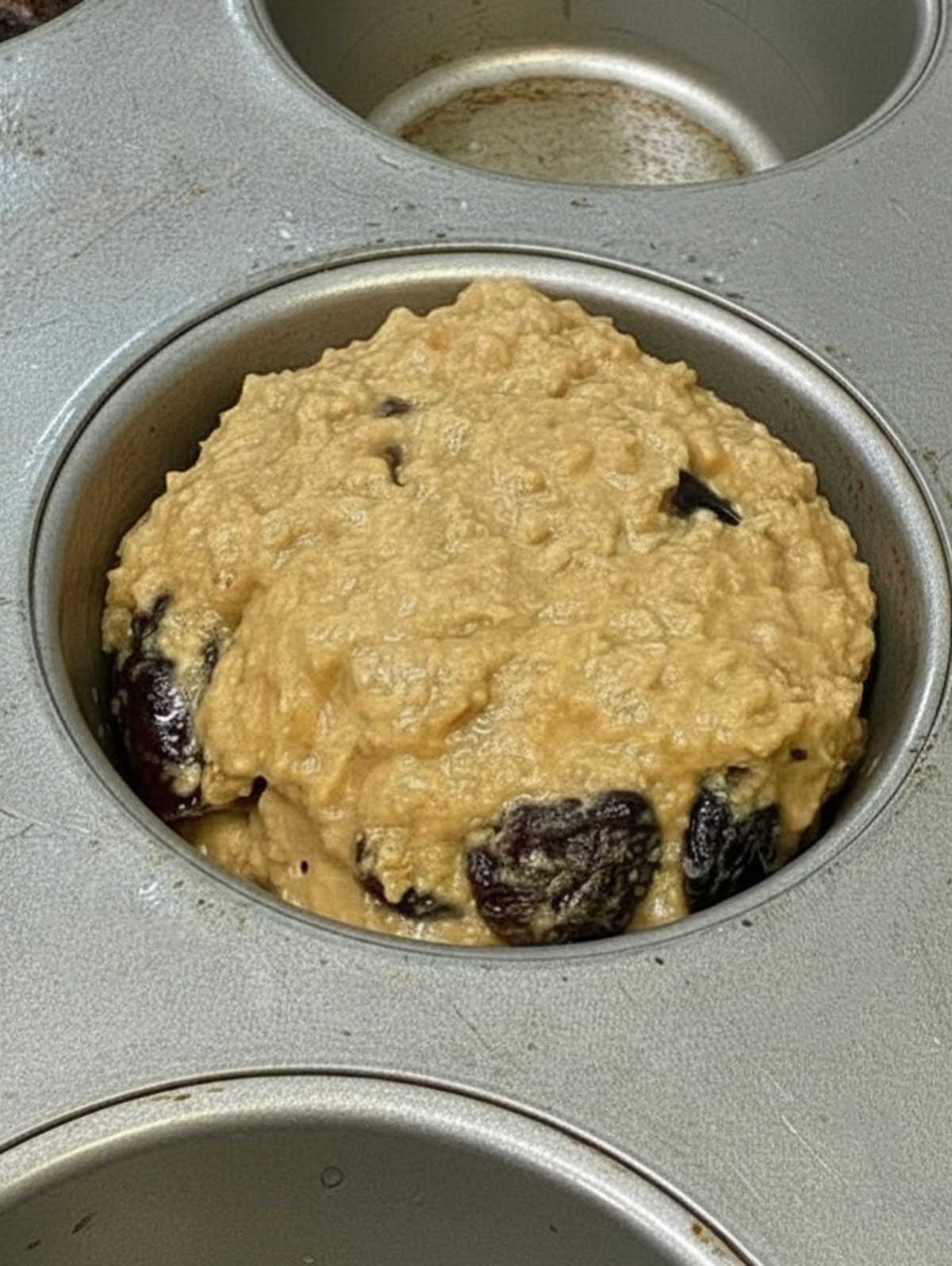 Bran muffin batter scooped into a cup showing thickness.
