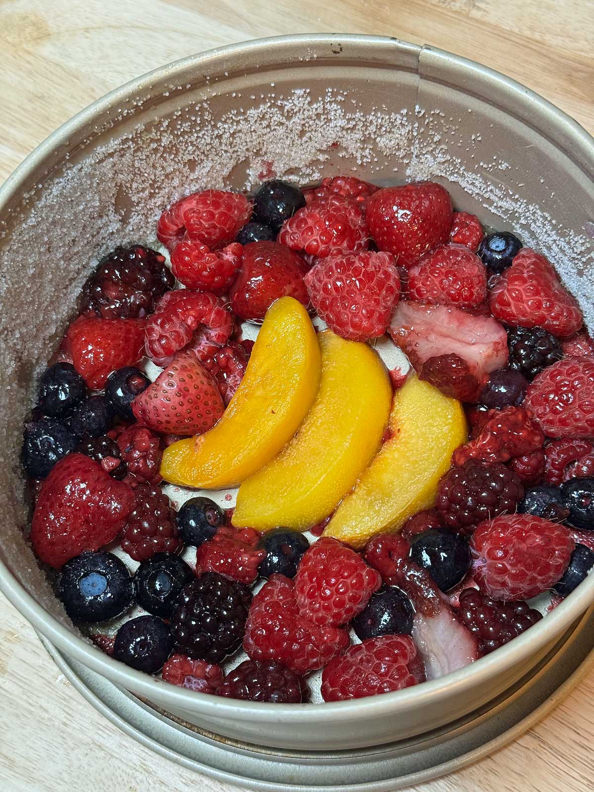 A springform pan greased with olive oil and dusted with granulated sugar with fruit on the bottom for an Upside Down Olive Oil Cake.