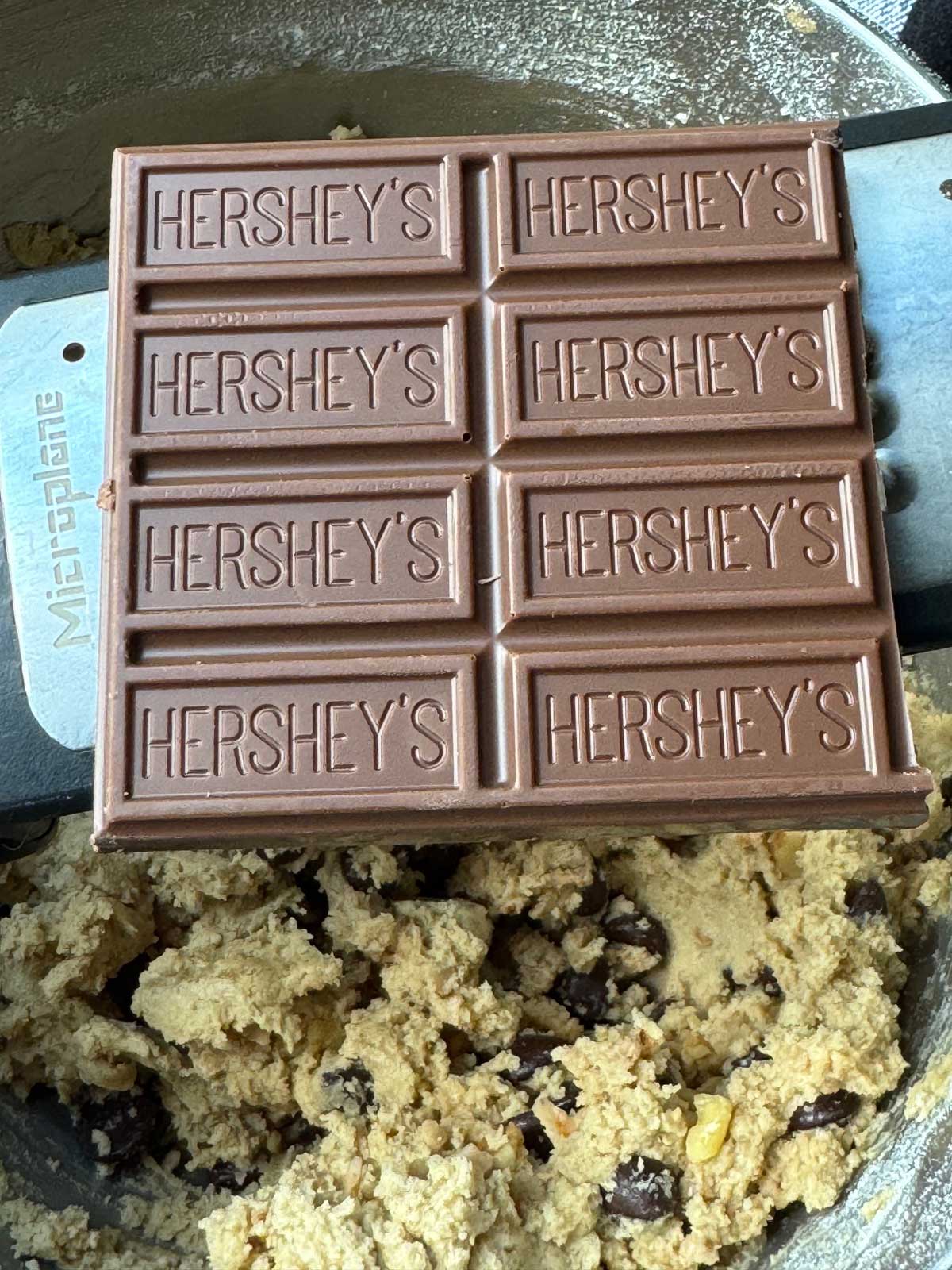 Hershey's Chocolate being grated into cookie dough to add sweetness.
