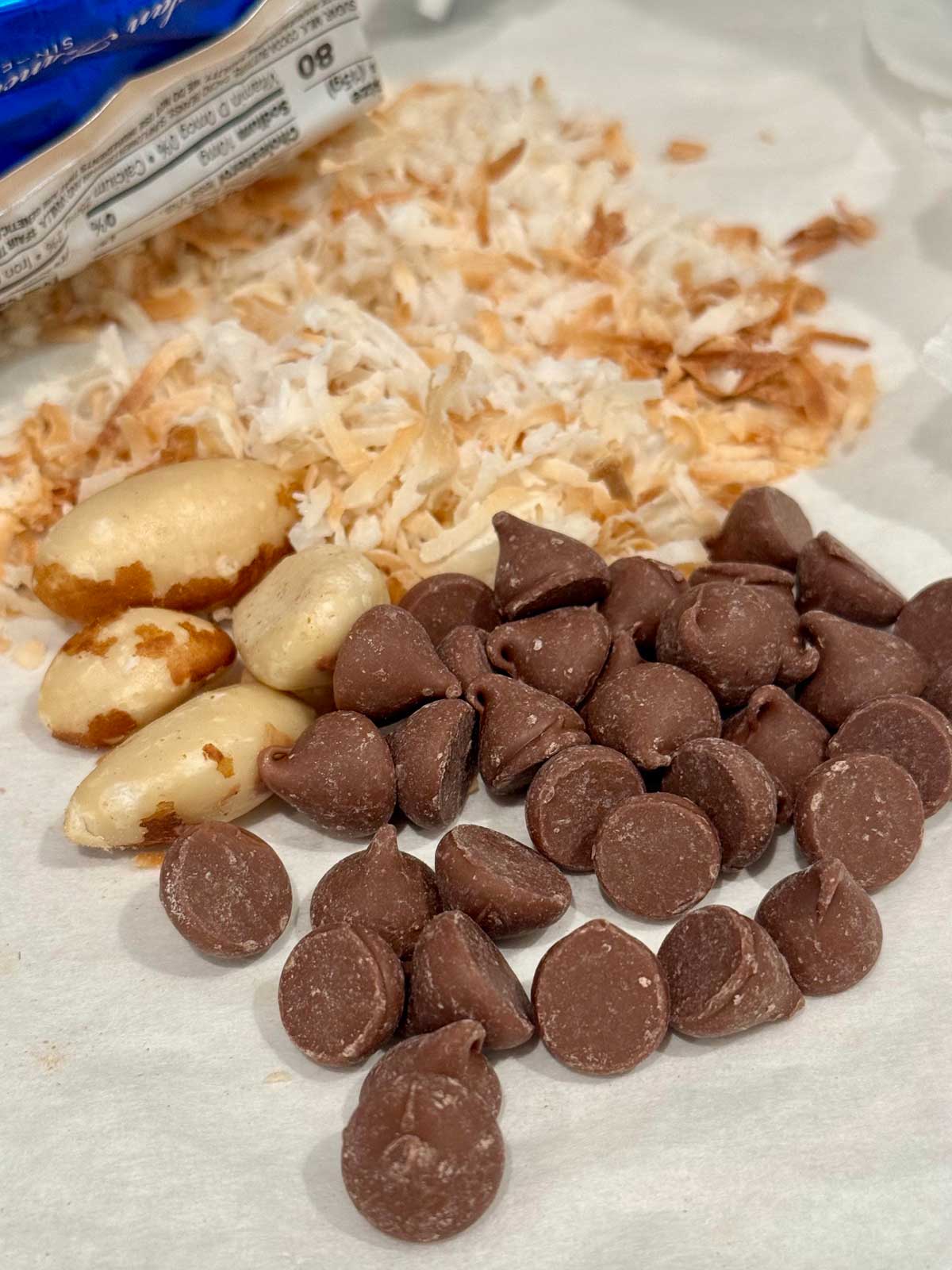 Brazil nuts, toasted coconut and Guittard chocolate chips on a piece of parchment for Toasted Coconut Chocolate Chunk Cookies.