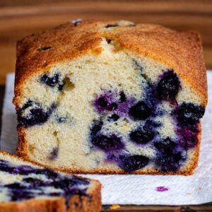 A lemon blueberry loaf cake with frozen fresh berries, sliced to show the crumb.