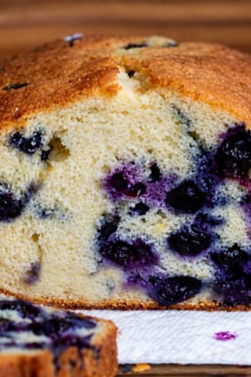 A lemon blueberry loaf cake with frozen fresh berries, sliced to show the crumb.