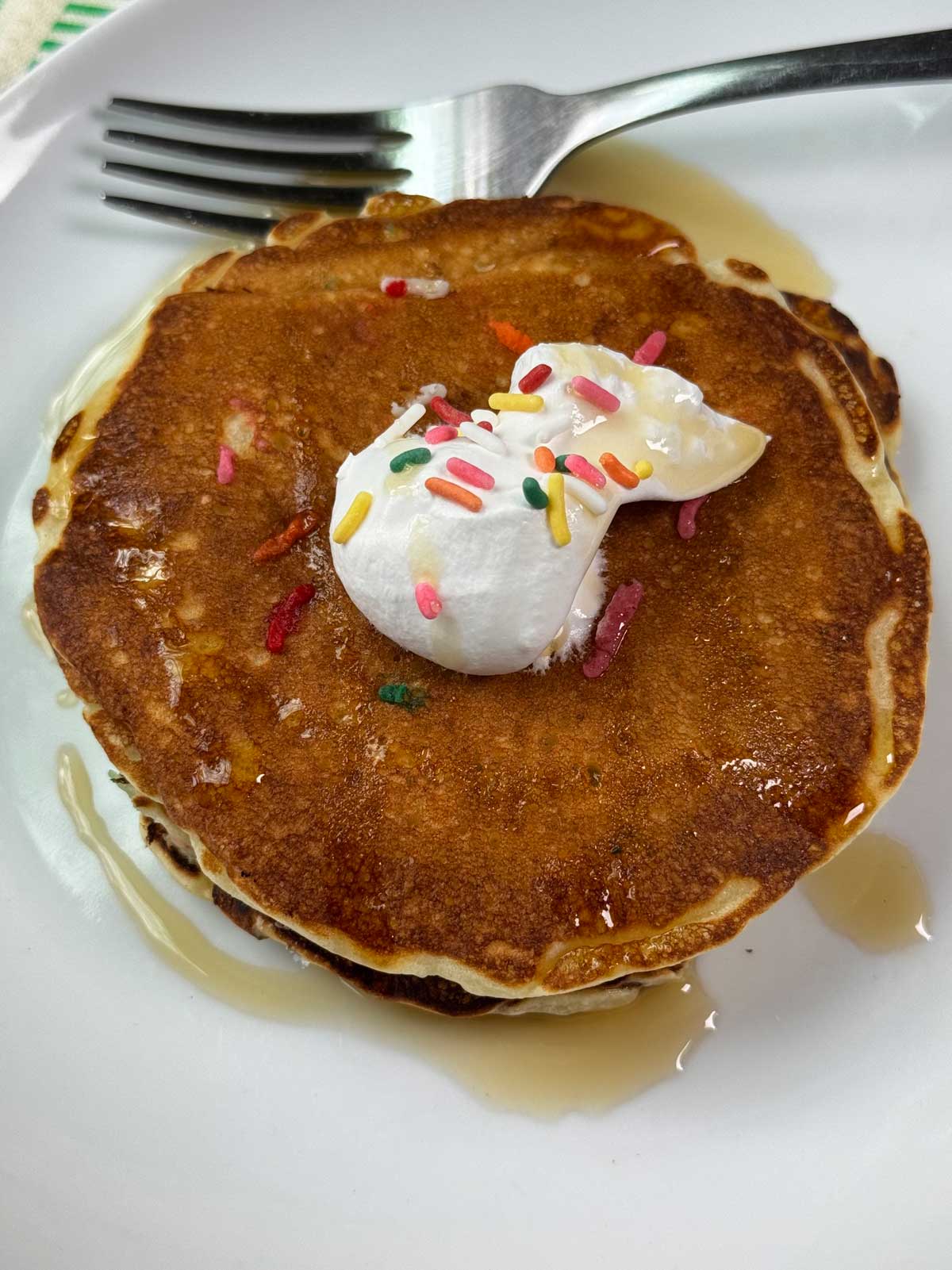 Malted Milk Powder Pancakes topped with sprinkles, whipped cream and maple syrup.