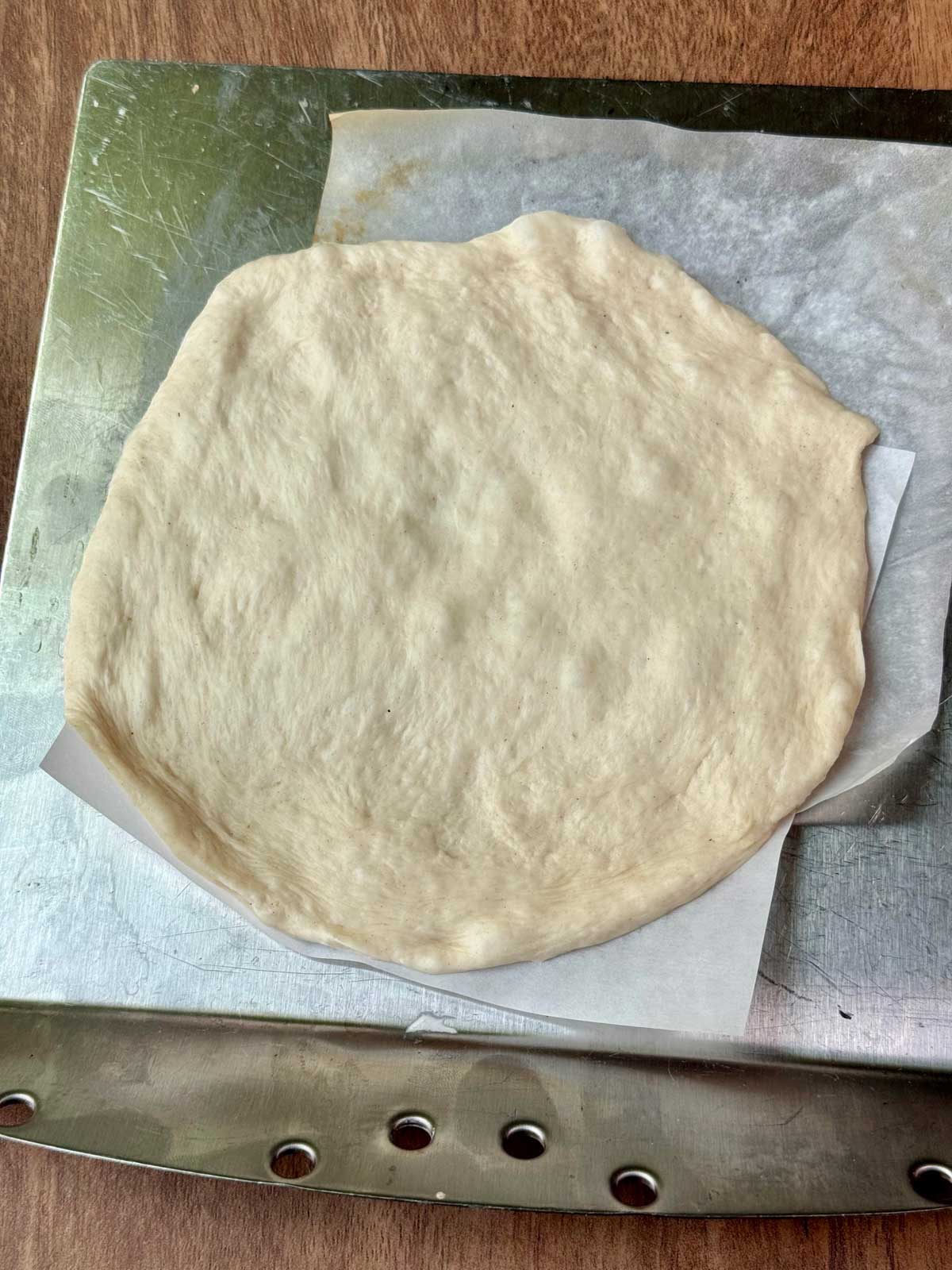 Pita pocket dough on parchment about to slide into the oven onto a hot stone.