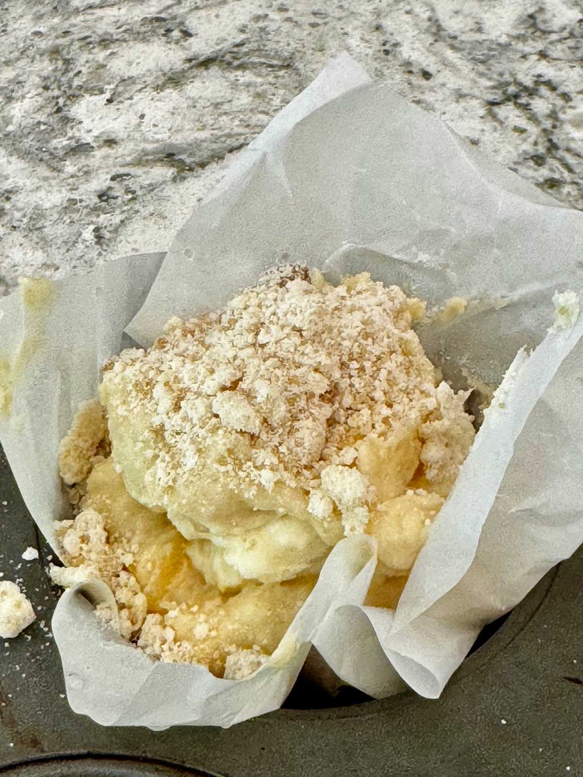 Muffin tin lined with parchment paper and pineapple muffin batter with streusel