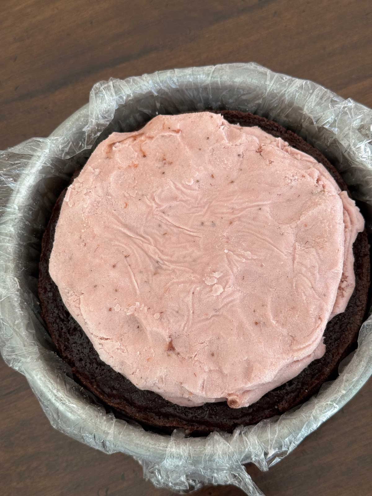 Strawberry ice cream mashed into a round and set on a frozen six inch chocolate cake to make an ice cream cake.