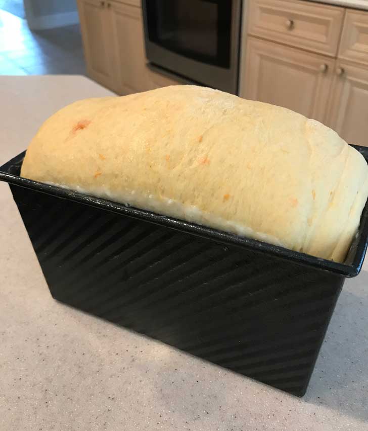 Sweet potato bread dough rising above the edge of a Pullman pan.