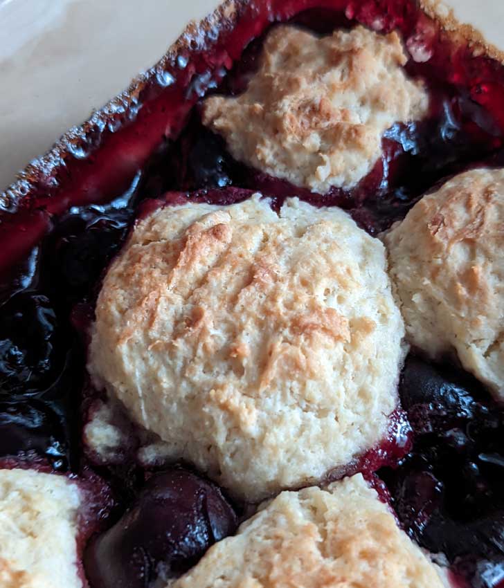 Close-up photo of a biscuit on top of cherry cobbler. Cherry Cobbler from The Food Allergy Baking Book.