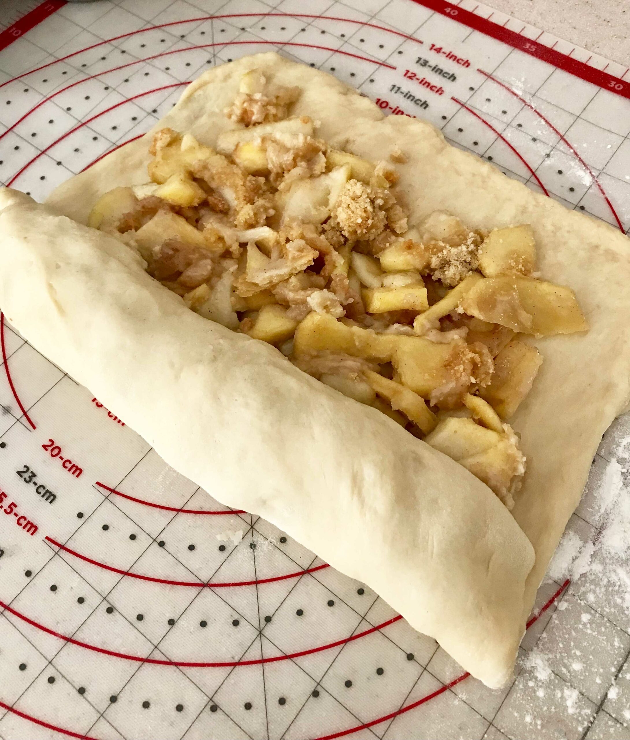 Dough with chopped up apple pie filling being rolled up to make cinnamon rolls.