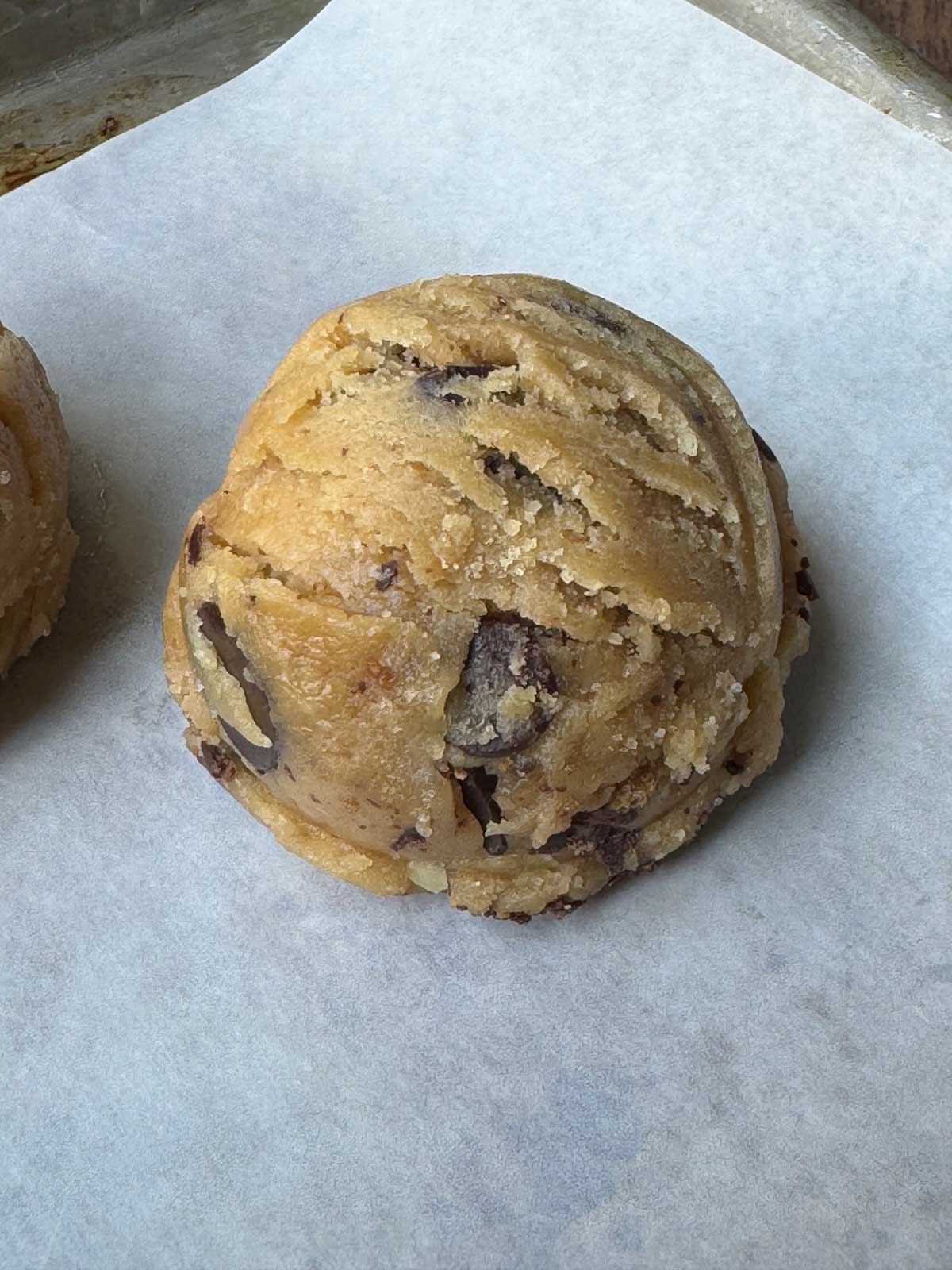 Chocolate chip cookie dough ball from a large cookie scoop on a sheet of parchment paper.