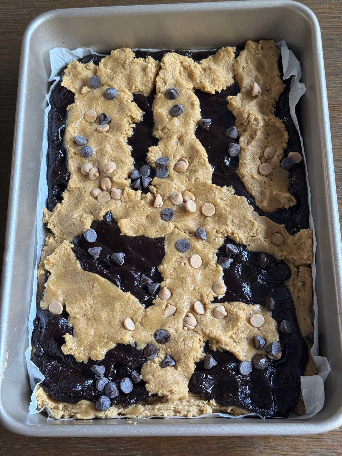 Unbaked peanut butter brookies in a pan showing how to layer the cookie dough and brownie batter.