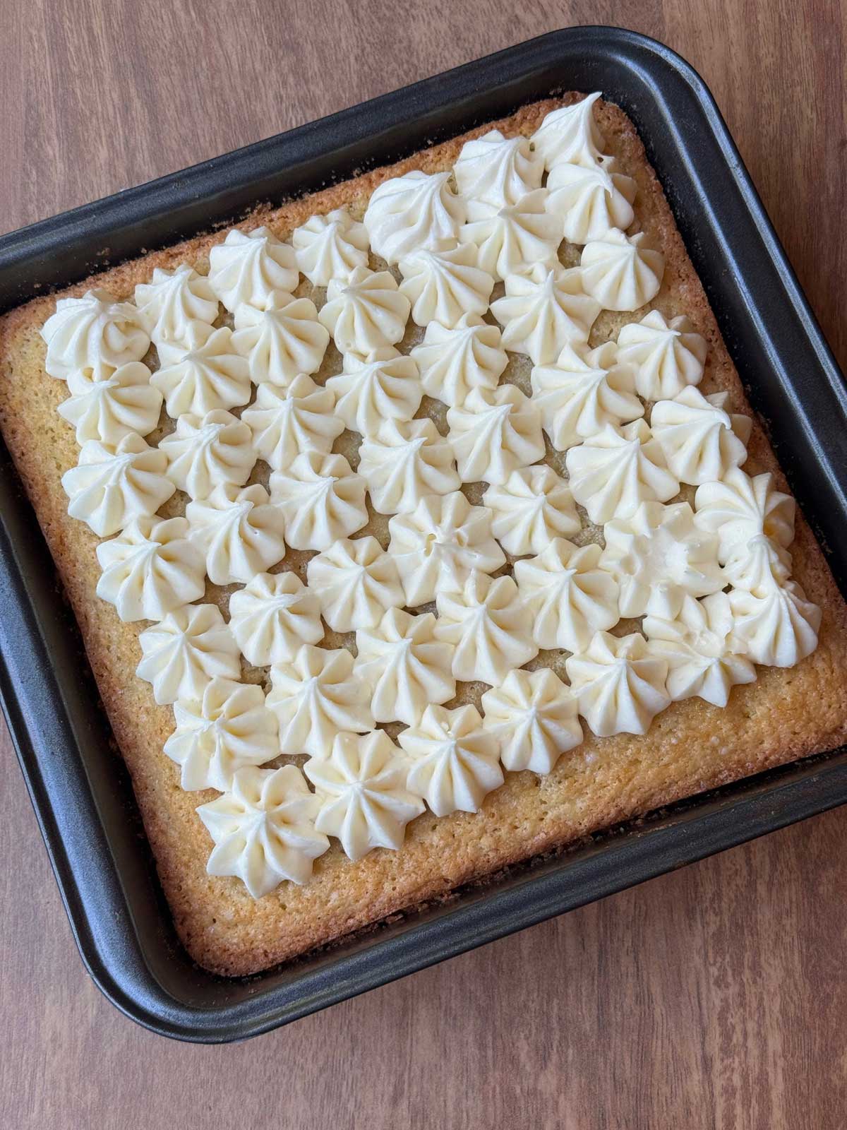 Key lime cake baked in an 8-inch square pan with cream cheese frosting piped on top.