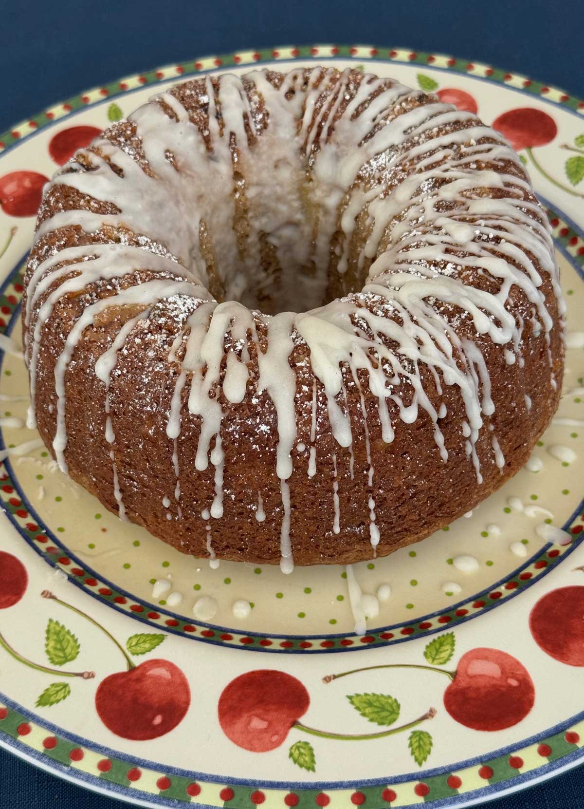 An apple flavored Bundt cake with a dusting of powdered sugar and a confectioners' sugar frosting.