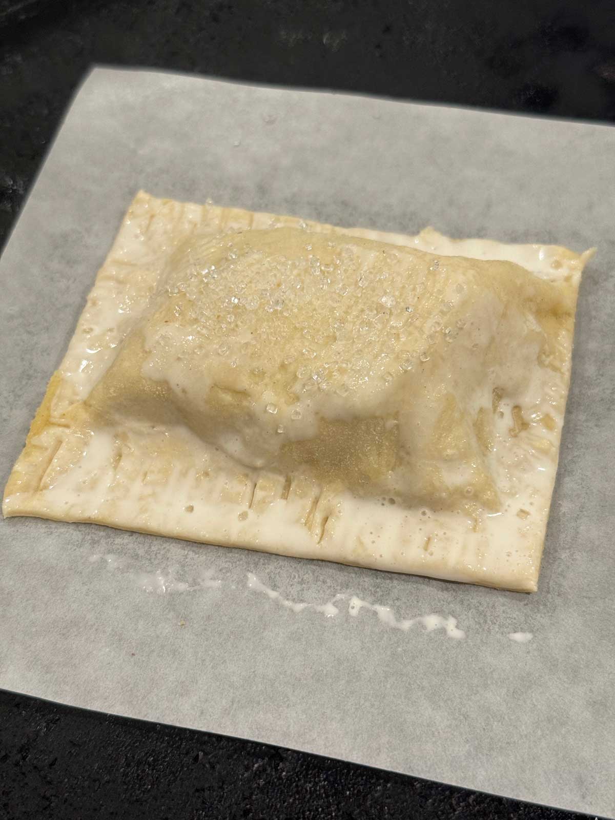 An unbaked apple hand pie brushed with cream.