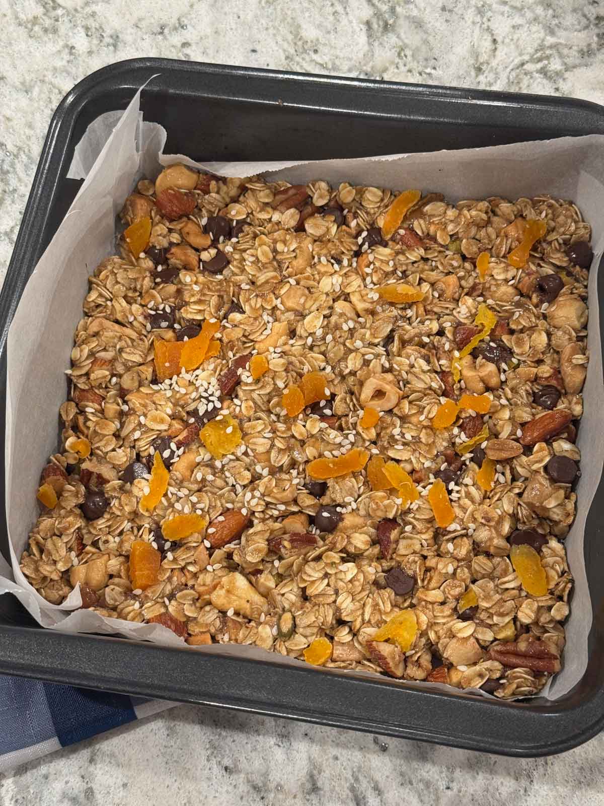 Unbaked Tahini Granola Bars pressed into a parchment lined 8-inch square pan.