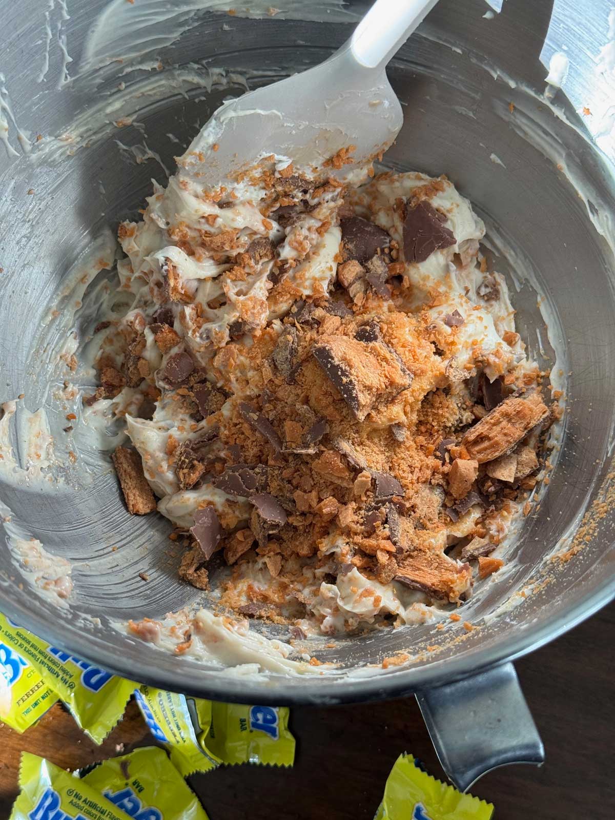 Butterfingers being folded into the filling for a Butterfinger Pie made with fresh whipped cream, cream cheese and a browned butter Ritz cracker crust.