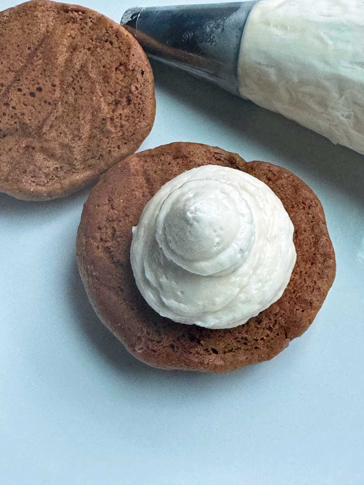 A gingerbread whoopie pie with filling piped out of a pastry bag.