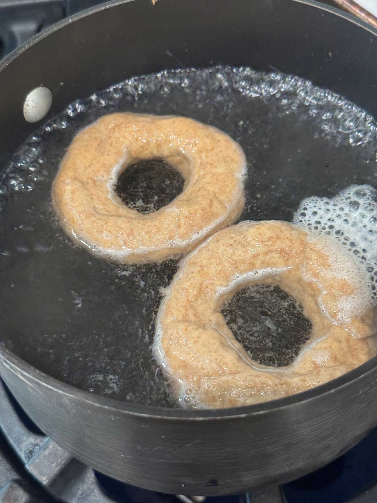 A pan of water with unbaked bagel dough boiling.