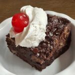 Chocolate Bread Pudding made with cubes of sourdough and topped with whipped cream and a cherry.