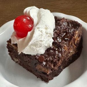 Chocolate Bread Pudding made with cubes of sourdough and topped with whipped cream and a cherry.