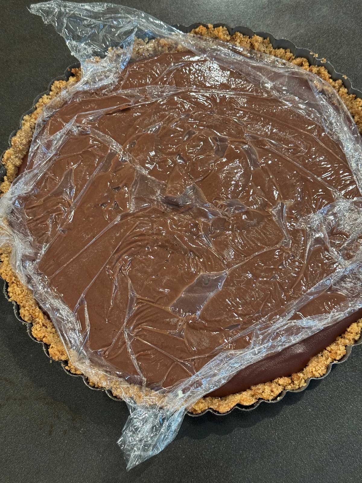 Graham cracker crust in a 9-inch tart pan filled with chocolate cream pudding waiting for topping.