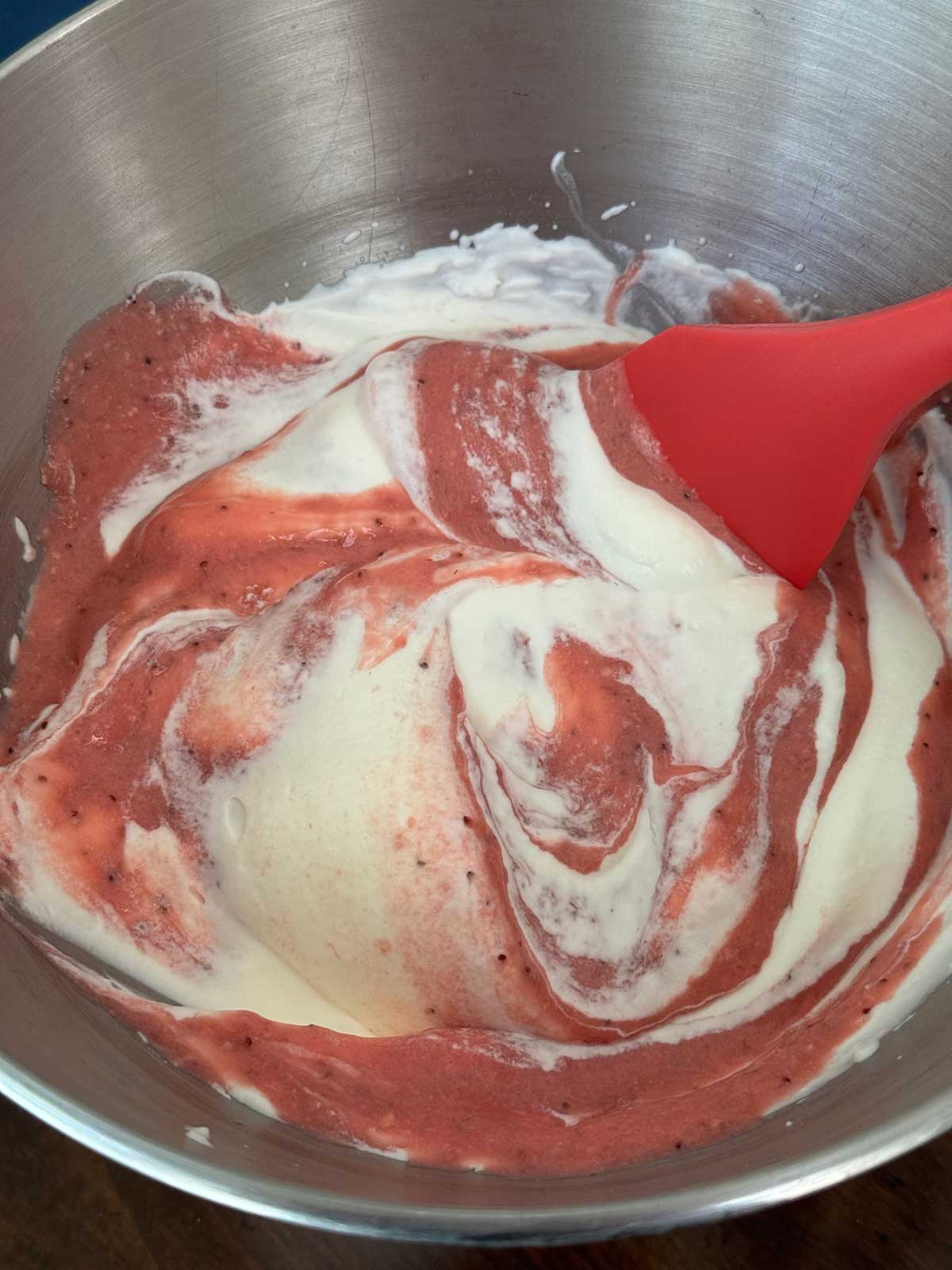 Whipped cream being folded into pureed strawberry mixture for strawberry pie.