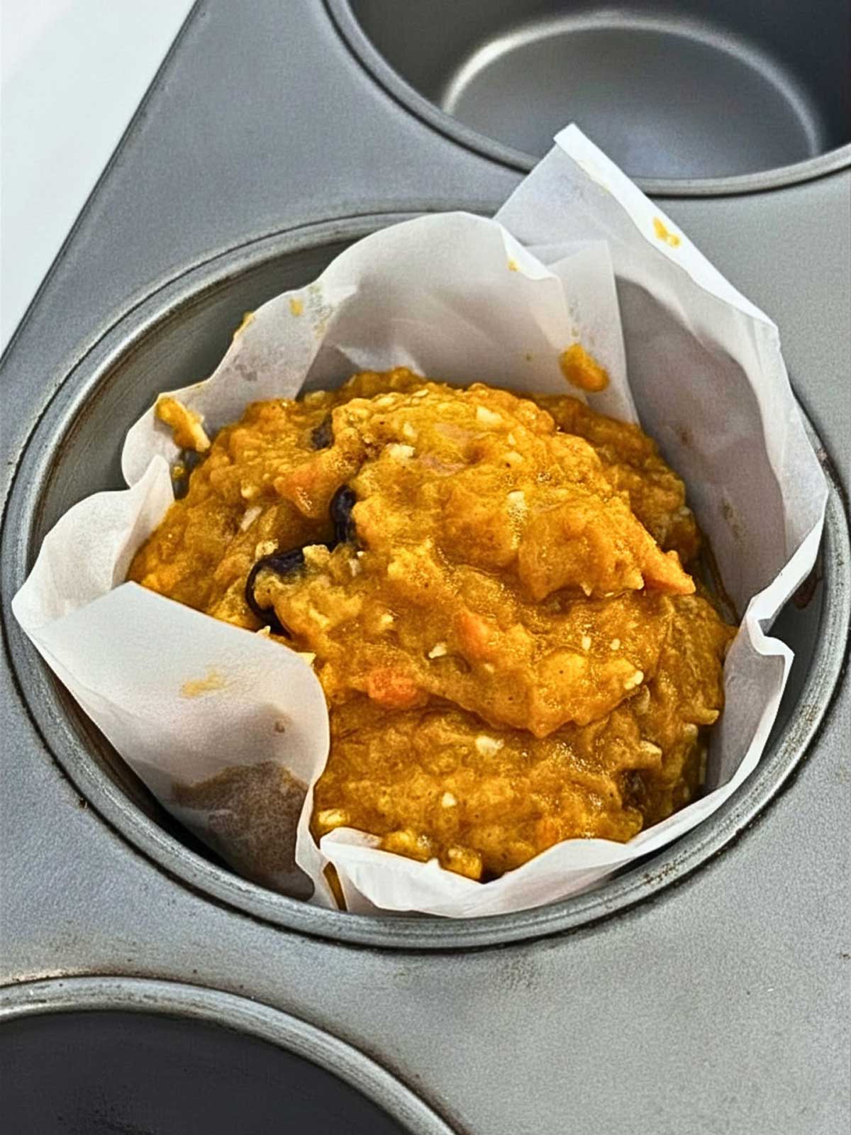 Carrot muffin batter inside a 5-inch parchment paper square lined muffin cup.