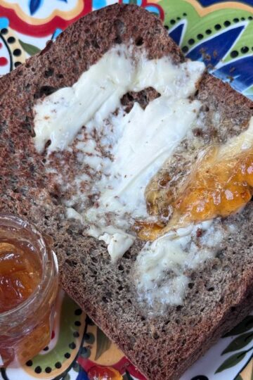 Dark buckwheat bread toasted and smeared with butter and orange marmalade.